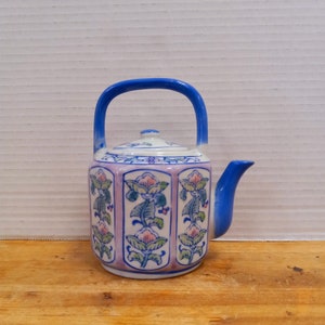 May include: A small blue and white teapot with a floral design. The teapot has a lid and a handle. The teapot is sitting on a wooden surface.