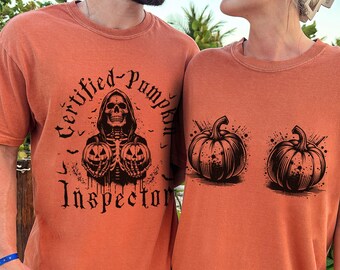 May include: Two orange t-shirts with a Halloween theme. The front of one shirt features a skeleton holding two pumpkins with the text "Certified Pumpkin Inspector". The other shirt has two pumpkins.