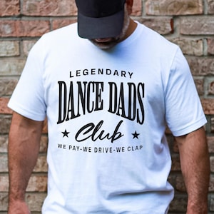 May include: White t-shirt with black text that reads "Legendary Dance Dads Club We Pay-We Drive-We Clap"