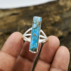 May include: A silver ring with a turquoise stone set in a rectangular shape. The stone has a blue and brown marbled pattern.
