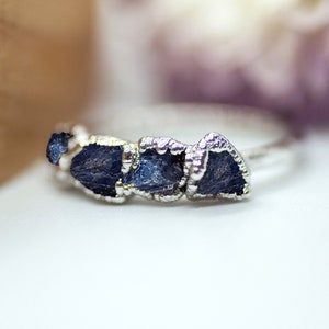 May include: A silver ring with four blue gemstone accents. The gemstones are rough and irregular in shape, giving the ring a unique and natural look.