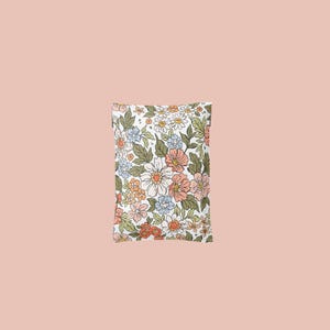 May include: A rectangular pillow with a floral pattern. The design features a white background with an array of flowers in shades of peach, orange, blue, and white, along with green leaves. The pillow is set against a solid pink background.