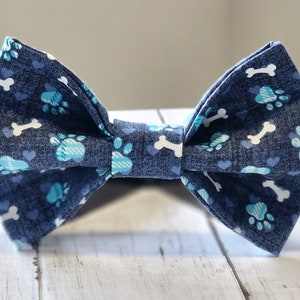 May include: A blue bow tie with a pattern of white bones and blue paw prints.
