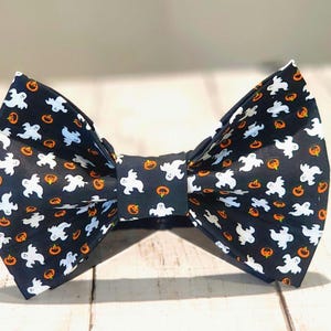 Könnte beinhalten: Schwarzer Fliege mit einem Halloween-Druck von weißen Geistern und orangefarbenen Kürbissen.