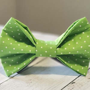 May include: A green bow tie with white polka dots. The bow tie is made of fabric and has a classic bow shape.