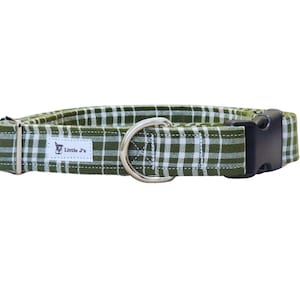 May include: A pet collar featuring a dark olive green and white plaid pattern. The collar includes a black plastic side-release buckle, a silver-toned metal D-ring, and a white fabric label with the text Little J's printed in black.