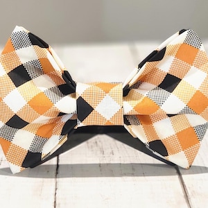 Könnte beinhalten: Eine schwarze, orange und weiße karierte Fliege. Die Fliege ist aus Stoff und hat eine klassische Schleifenform.