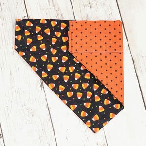 Puede incluir: Un bandana para perro negro y naranja con un patrón de maíz dulce y lunares.