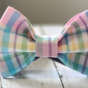 May include: A pastel plaid bow tie with pink, blue, yellow, and green colors. The bow tie is tied and ready to wear.