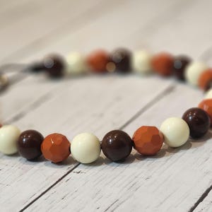 May include: A brown, white, and orange beaded necklace with a silver clasp.