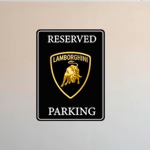 Puede incluir: Cartel rectangular negro con texto blanco &laquo;&nbsp;RESERVED PARKING&nbsp;&raquo;. El centro presenta el logotipo de Lamborghini en oro, un escudo con un toro dorado. El cartel tiene un borde negro.