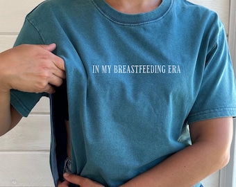 May include: A teal blue t-shirt with the text "IN MY BREASTFEEDING ERA" printed in white on the front.