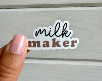 May include: A white sticker with the text "milk maker" in black and brown lettering. The sticker is being held by a finger.