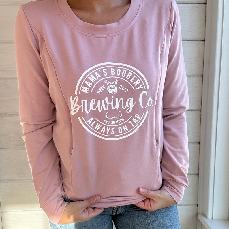 Beige Crewneck Sweatshirt with a logo in black Mama Boobery Brewing Co. Always on Tap 24/7 Two Locations. Breastfeeding Friendly Sweatshirt with zippers on either side that zip from the bottom up for easy accessibility to latch baby to nurse.