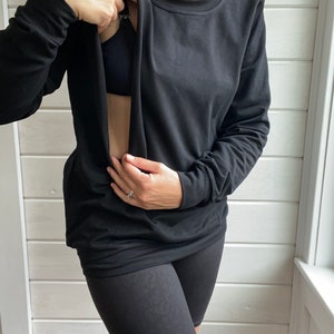 May include: A black long-sleeved shirt with a built-in nursing panel, allowing for easy breastfeeding access. The shirt is worn with black biker shorts.