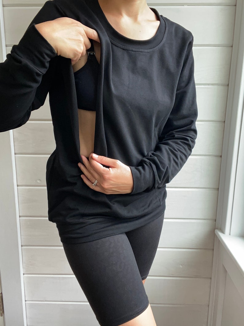 May include: A black long-sleeved shirt with a built-in nursing panel, allowing for easy breastfeeding access. The shirt is worn with black biker shorts.