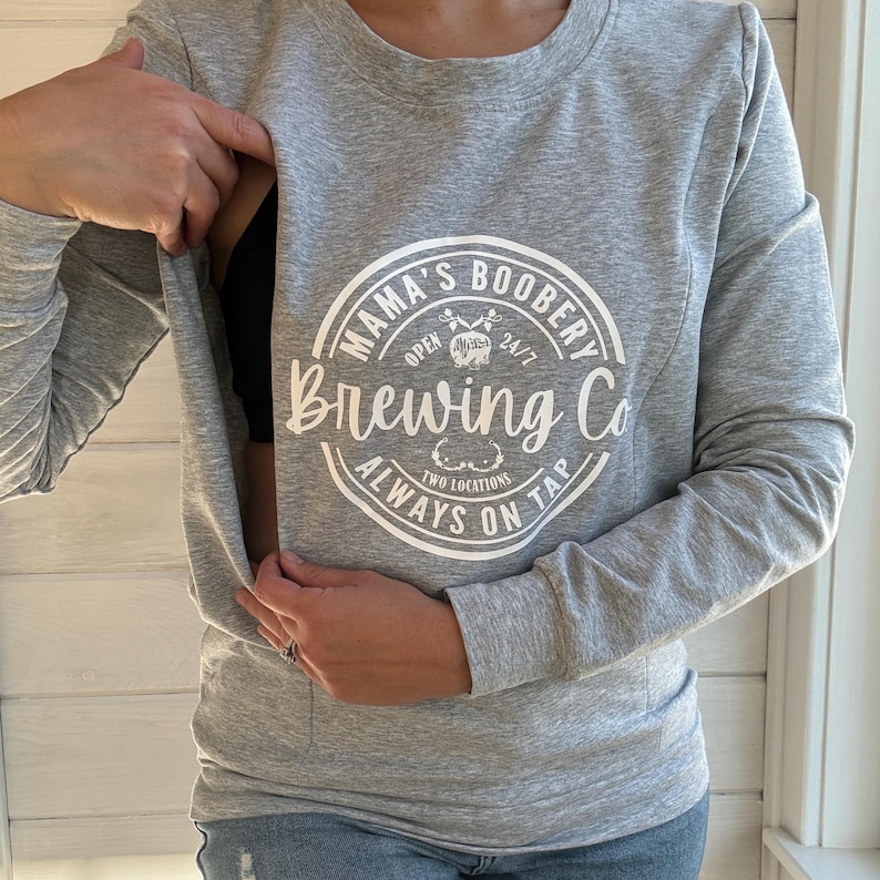 Beige Crewneck Sweatshirt with a logo in black Mama Boobery Brewing Co. Always on Tap 24/7 Two Locations. Breastfeeding Friendly Sweatshirt with zippers on either side that zip from the bottom up for easy accessibility to latch baby to nurse.