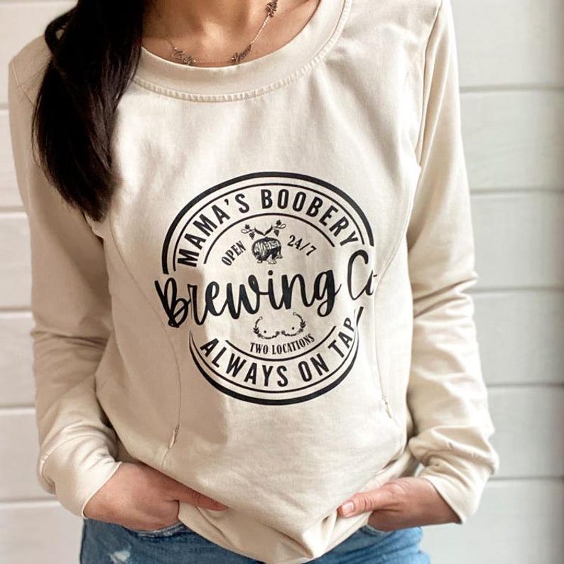 Beige Crewneck Sweatshirt with a logo in black Mama Boobery Brewing Co. Always on Tap 24/7 Two Locations. Breastfeeding Friendly Sweatshirt with zippers on either side that zip from the bottom up for easy accessibility to latch baby to nurse.