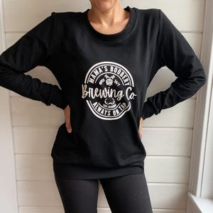 Beige Crewneck Sweatshirt with a logo in black Mama Boobery Brewing Co. Always on Tap 24/7 Two Locations. Breastfeeding Friendly Sweatshirt with zippers on either side that zip from the bottom up for easy accessibility to latch baby to nurse.