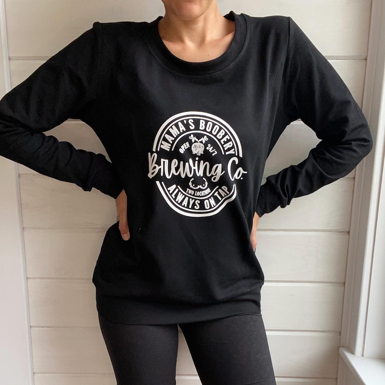 Beige Crewneck Sweatshirt with a logo in black Mama Boobery Brewing Co. Always on Tap 24/7 Two Locations. Breastfeeding Friendly Sweatshirt with zippers on either side that zip from the bottom up for easy accessibility to latch baby to nurse.