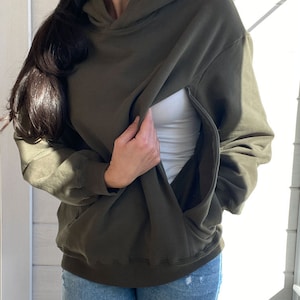 Pu&ograve; includere: Una felpa con cappuccio verde scuro con una cerniera nascosta per un facile allattamento al seno. La felpa &egrave; mostrata indossata con una canottiera bianca e jeans blu.