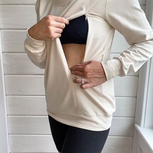May include: A cream colored long-sleeved shirt with a zipper opening at the chest. The shirt is made of a soft, stretchy fabric and has a relaxed fit.