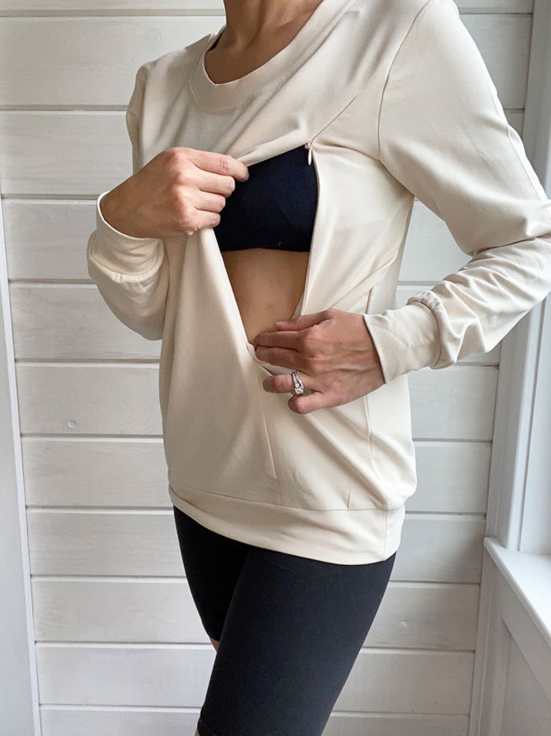 May include: A cream colored long-sleeved shirt with a zipper opening at the chest. The shirt is made of a soft, stretchy fabric and has a relaxed fit.