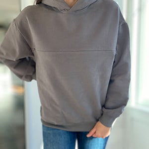 Pu&ograve; includere: Una felpa con cappuccio grigia con una vestibilit&agrave; rilassata. La felpa ha una singola cucitura sul petto.