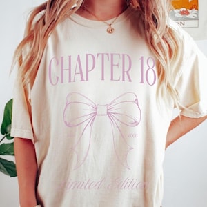 May include: Ivory-colored t-shirt with the text "CHAPTER 18" in a light purple font, along with a bow graphic. The words "Limited Edition" and the year "2008" are also printed on the shirt. The shirt is a casual style.