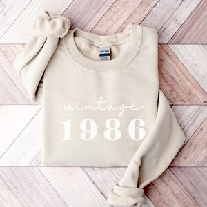 May include: A beige sweatshirt with the text "vintage 1986" printed in white.