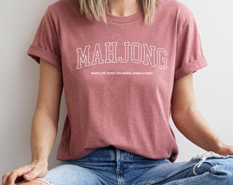 May include: A heather mauve t-shirt with the text "Mahjong" in white outlined letters. The text "When life gives you winds, make a pung" is printed below the word "Mahjong".