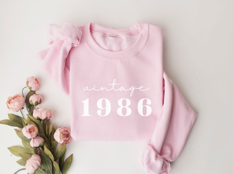 May include: Pink sweatshirt with the text "vintage 1986" in white.