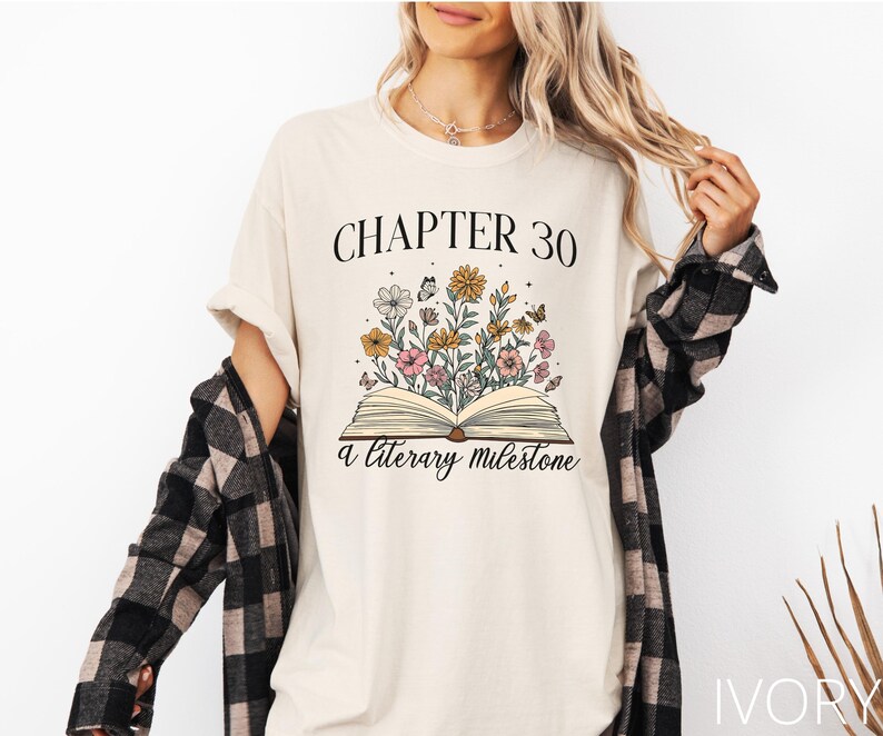May include: A white t-shirt with the text "Chapter 30 A Literary Milestone" and a floral illustration of a book with flowers.