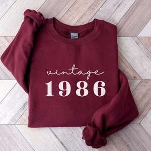May include: Burgundy sweatshirt with the text "vintage 1986" in white.