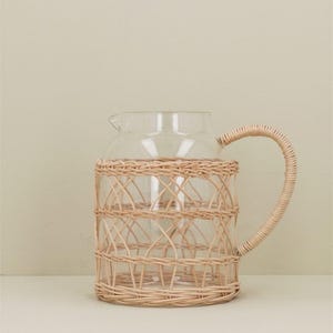 May include: A clear glass pitcher with a woven wicker handle and body. The wicker is a light brown colour.
