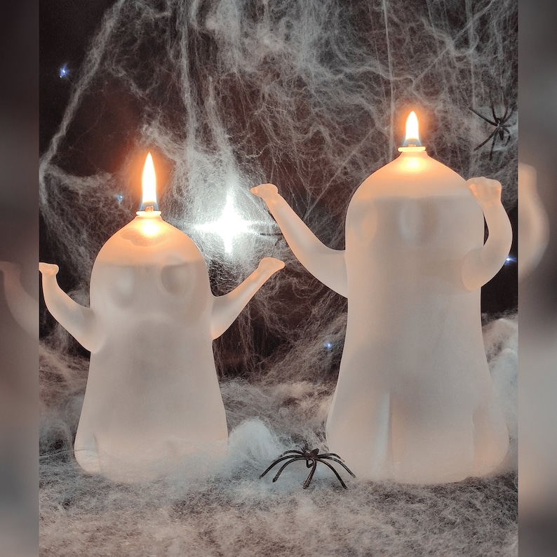 K&ouml;nnte beinhalten: Zwei wei&szlig;e, geisterf&ouml;rmige &Ouml;llampen mit brennenden Flammen im Inneren. Die Lampen stehen auf einer wei&szlig;en, spinnennetzartigen Oberfl&auml;che.