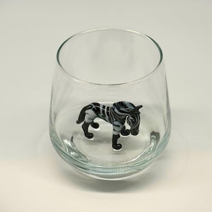 May include: A clear, stemless wine glass with a decorative, miniature zebra figurine inside. The zebra is black and white with a striped pattern. The glass has a wide, rounded shape.