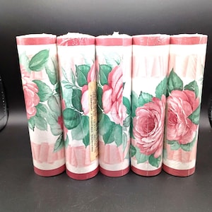 Puede incluir: Cinco rollos de papel pintado con un diseño floral de rosas. El papel pintado tiene un fondo blanco con rosas rosas, hojas verdes y un borde rosa y rojo. Una etiqueta con texto es visible en un rollo.
