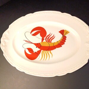 Puede incluir: Plato ovalado blanco para servir con un diseño de langosta roja, naranja y amarilla. El plato tiene un borde festoneado decorativo. Una pieza encantadora para servir comida, con temática de mariscos.