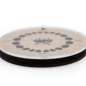 May include: A wooden baby teeth tracker with a clear acrylic cover. The tracker has a circle of 20 small black circles to mark the baby teeth. The text "Travo Baby Teeth" is printed on the tracker. The text "Lower" is printed below the circle of black circles.