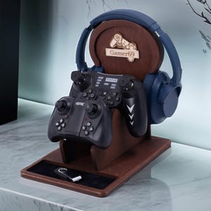 May include: A wooden gaming headset and controller stand. The stand is brown with a circular back and a small tray. A blue headset and two black controllers are displayed. The stand has the text "Gamer69". A USB drive is in the tray.