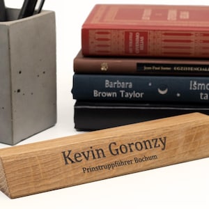 Op de afbeelding: Een houten bureau naamplaatje met de tekst "Kevin Goronzy" en "Prinstruppführer Bochum" erop gegraveerd.