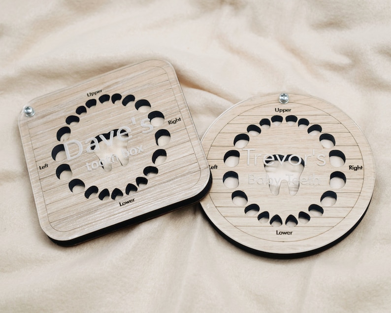 May include: Two wooden tooth boxes with a circular and square shape. The boxes are made of light brown wood with a wood grain pattern. The boxes have a cutout of a tooth in the center and are labeled with the names "Dave's Tooth Box" and "Trevor's Baby Teeth".