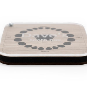 May include: A wooden tooth box with a clear acrylic top. The box has a gray circle with the text "Dave's Tooth Box" and a diagram of teeth. The box has a black border.
