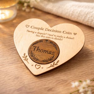 Puede incluir: Una moneda de decisión de pareja de madera en forma de corazón con el nombre "Thomas" grabado en un inserto circular. La moneda tiene el texto "¿Tienes una disputa? ¿Necesitas tomar una decisión? ¡Usa esta moneda para decidir!"