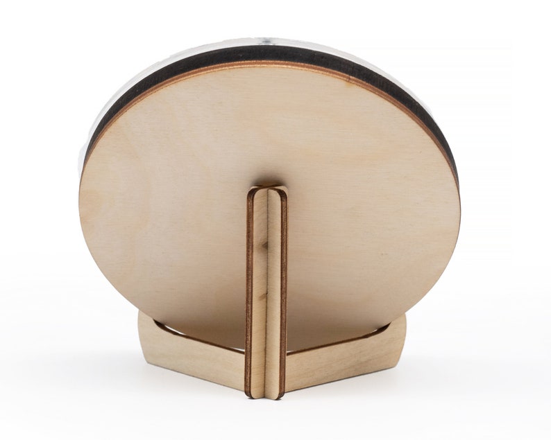 May include: A round wooden plaque with a stand. The plaque is light brown and has a dark brown edge. The stand is made of the same wood and has a triangular shape.
