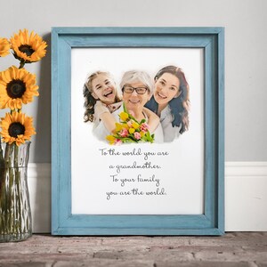 May include: A framed print featuring a watercolour-style photograph of three generations of women, a grandmother, mother, and daughter, with a quote that reads "To the world you are a grandmother. To your family you are the world."