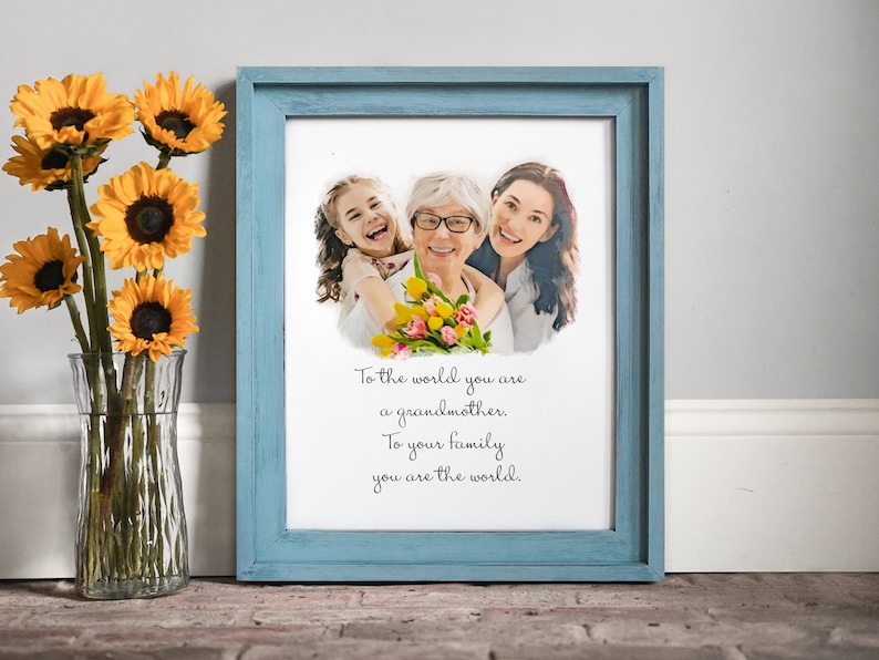 May include: A framed print featuring a watercolour-style photograph of three generations of women, a grandmother, mother, and daughter, with a quote that reads "To the world you are a grandmother. To your family you are the world."