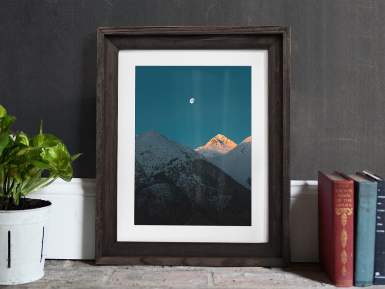 Puede incluir: Una fotograf&iacute;a enmarcada de una cordillera con luna llena en el cielo. Las monta&ntilde;as est&aacute;n cubiertas de nieve y el cielo es de un azul profundo.