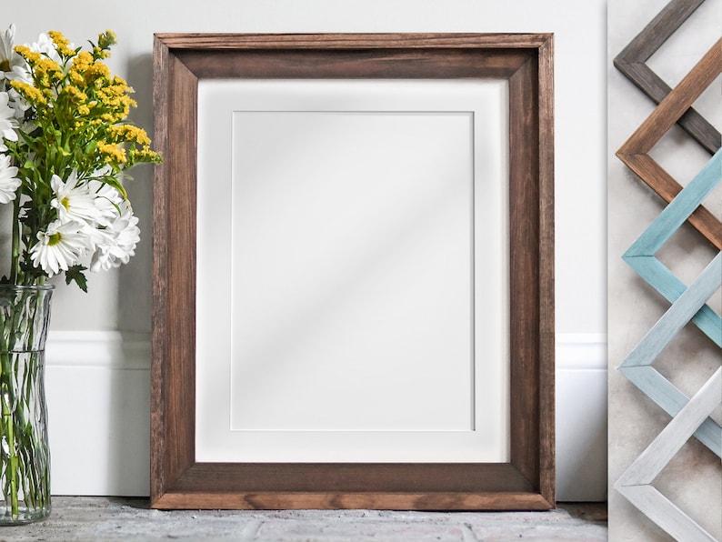 Puede incluir: Un marco de madera marr&oacute;n con un paspart&uacute; blanco y un fondo blanco. El marco est&aacute; sobre una superficie gris.